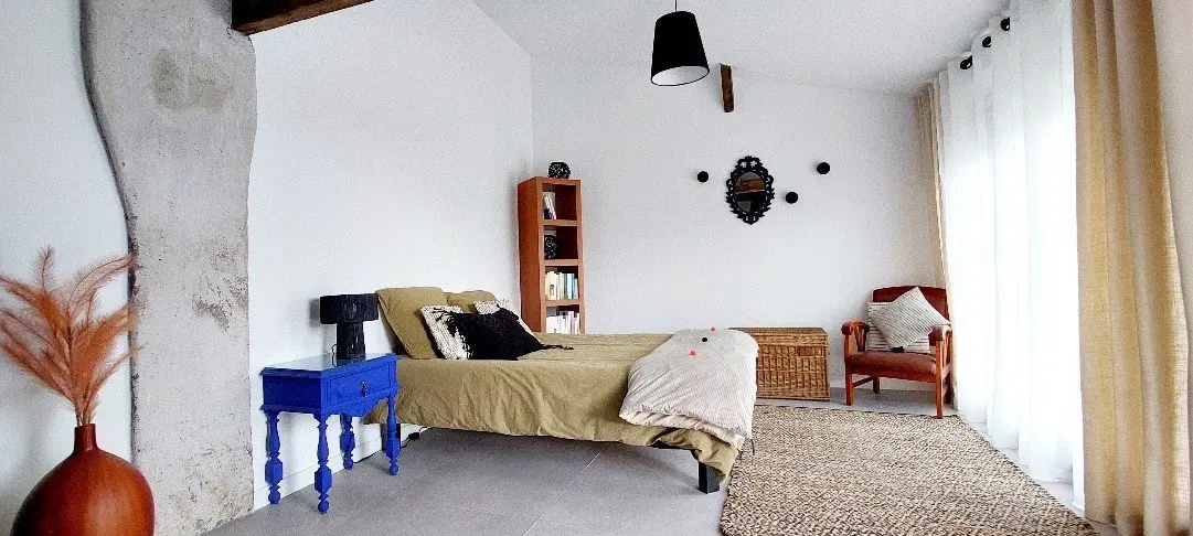 Chambre du gîte avec lit double, table de chevet et fauteuil.